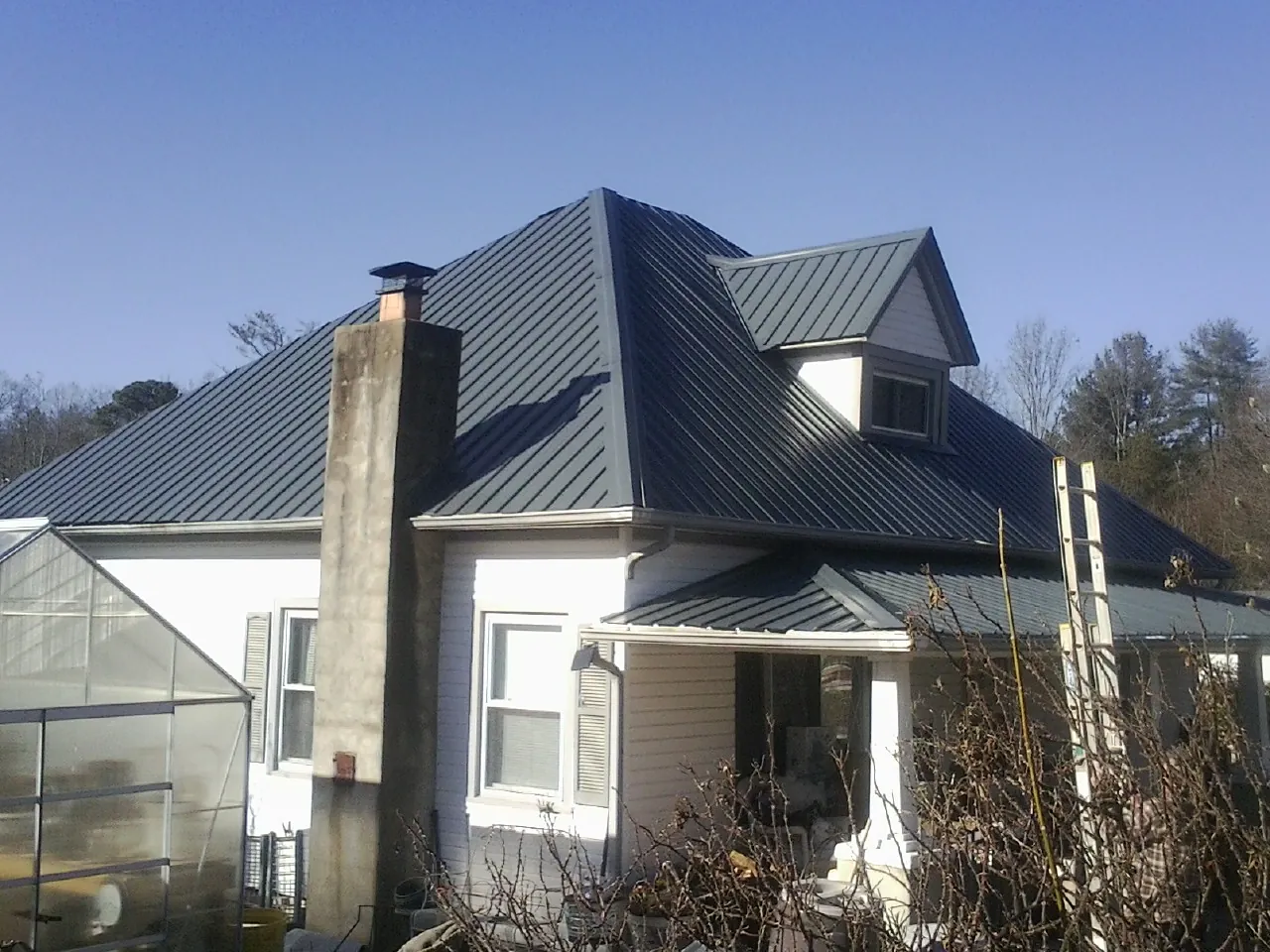 Dark blue standing seam metal roof on a white farmhouse with dormer — Slate & Tile Roof Repair by Roofing Brothers in Glendale Springs