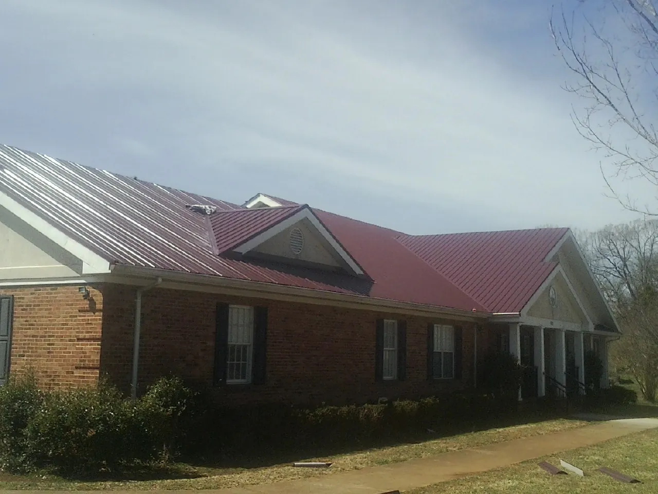 Red metal roof with gabled entries on a long brick building, from a Hail Damage Roof Repair job in Glendale Springs