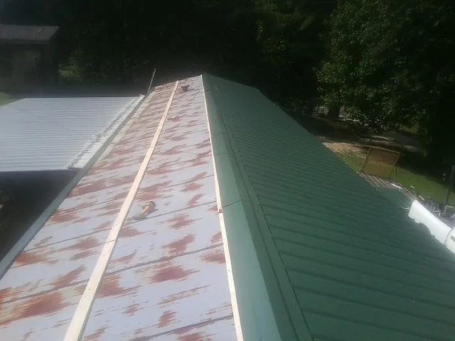 Old rusted panels beside newly installed green metal roofing — Wind Damage Roof Repair by Roofing Brothers in Glendale Springs