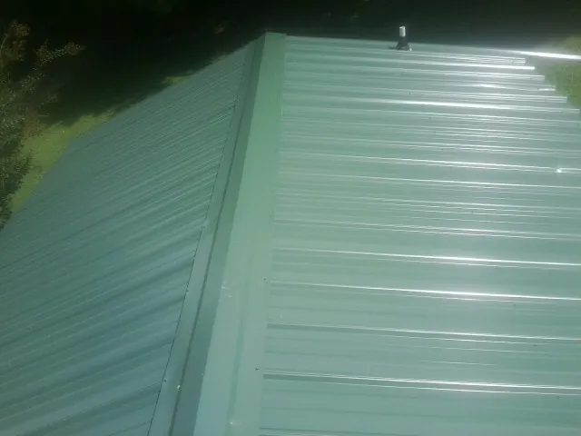New green metal panels meeting at the ridge of a roof — Flat Roof Repair work by our crew in Glendale Springs