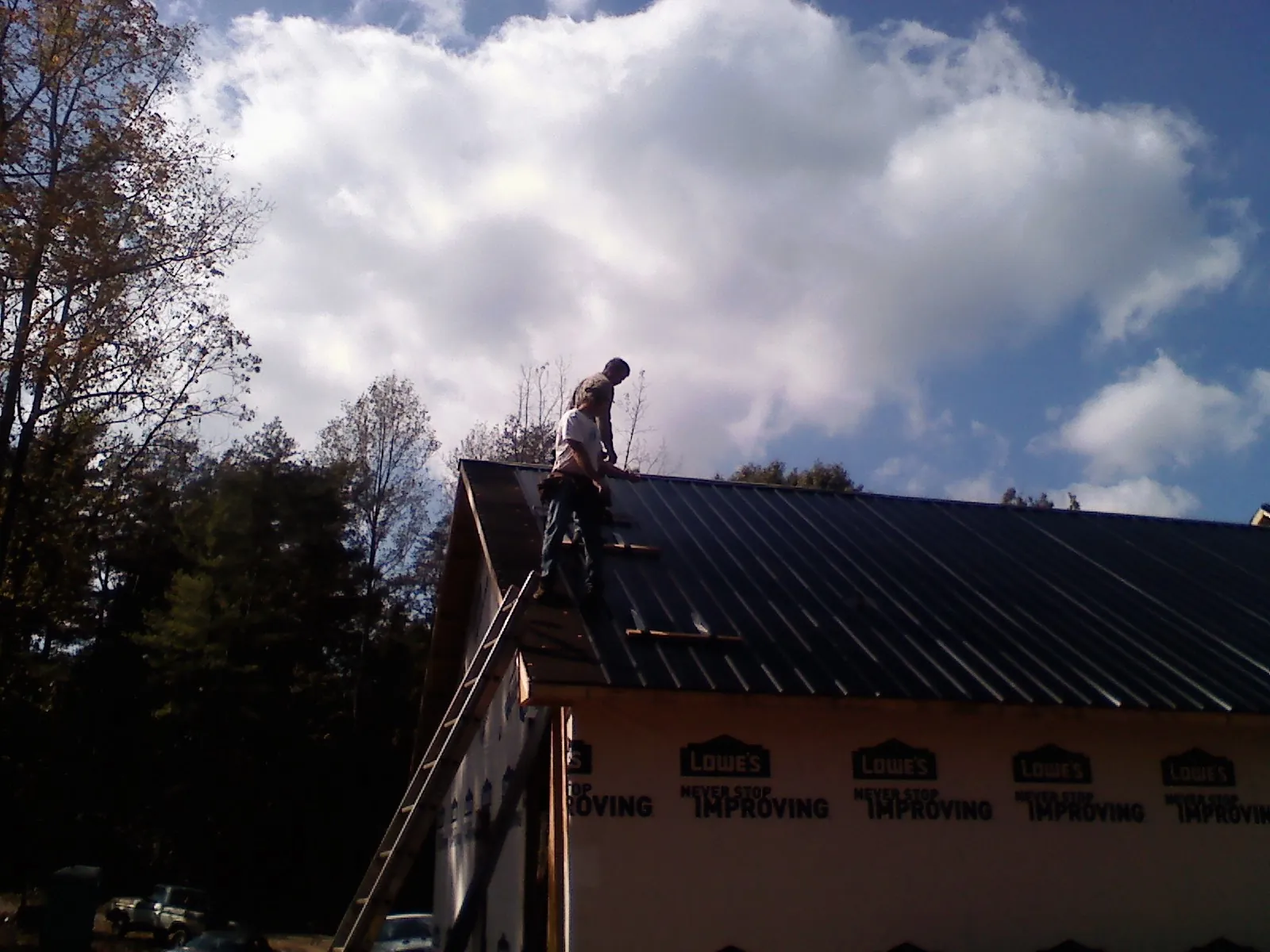 Roofer fastening dark metal panels high against a cloudy sky, from a Roof Inspection job in Glendale Springs