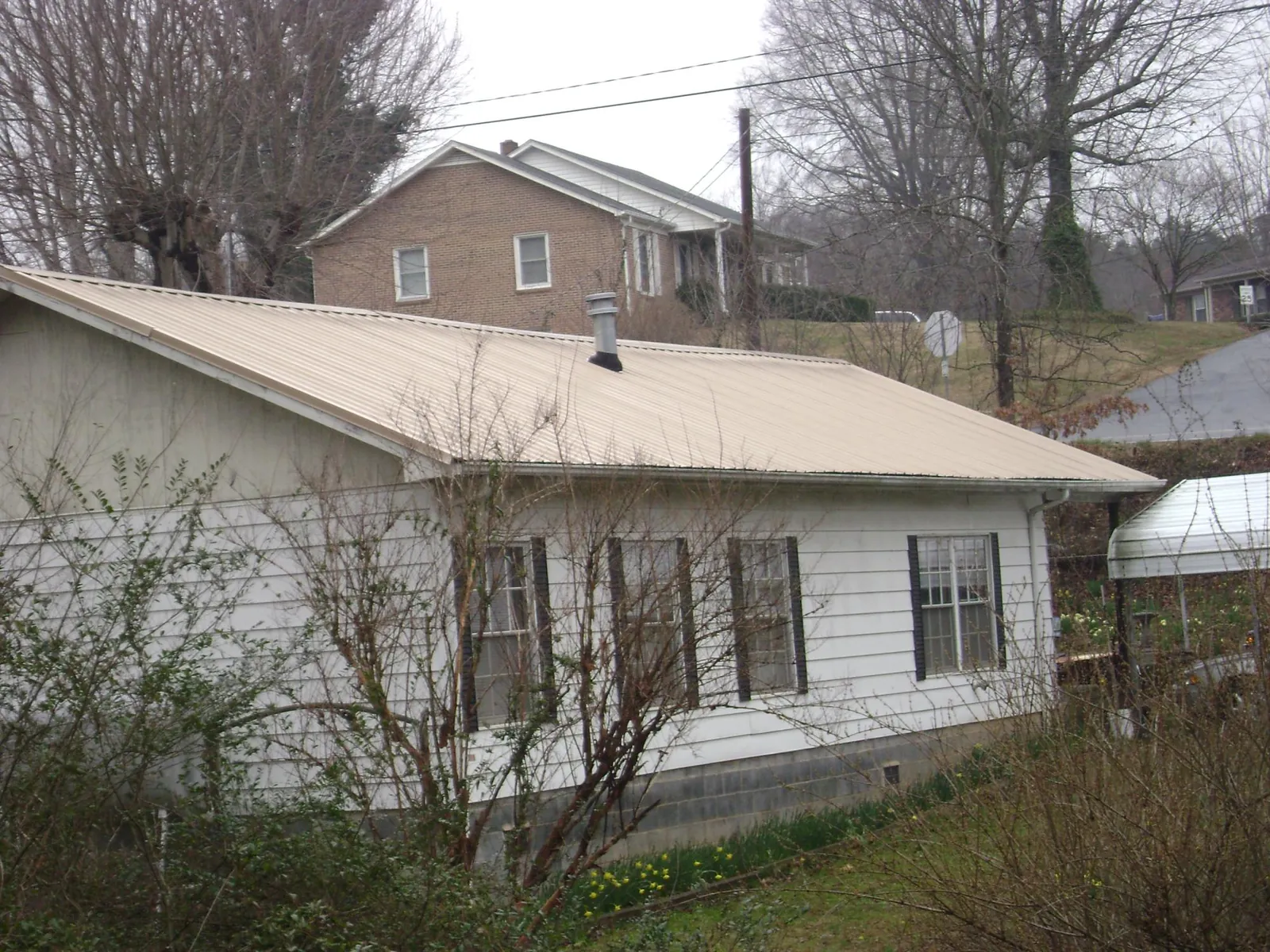 Tan metal roof on a white sided house set into a hillside — Commercial Roofing by Roofing Brothers in Glendale Springs